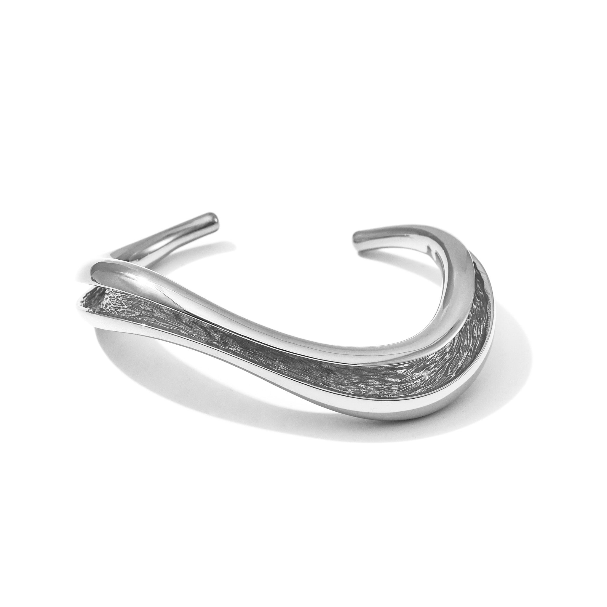 An open cuff that captures Currents at its clearest — a smooth, wave-like outer surface hiding a textured channel within. Slips on and gently adjusts to the wrist.