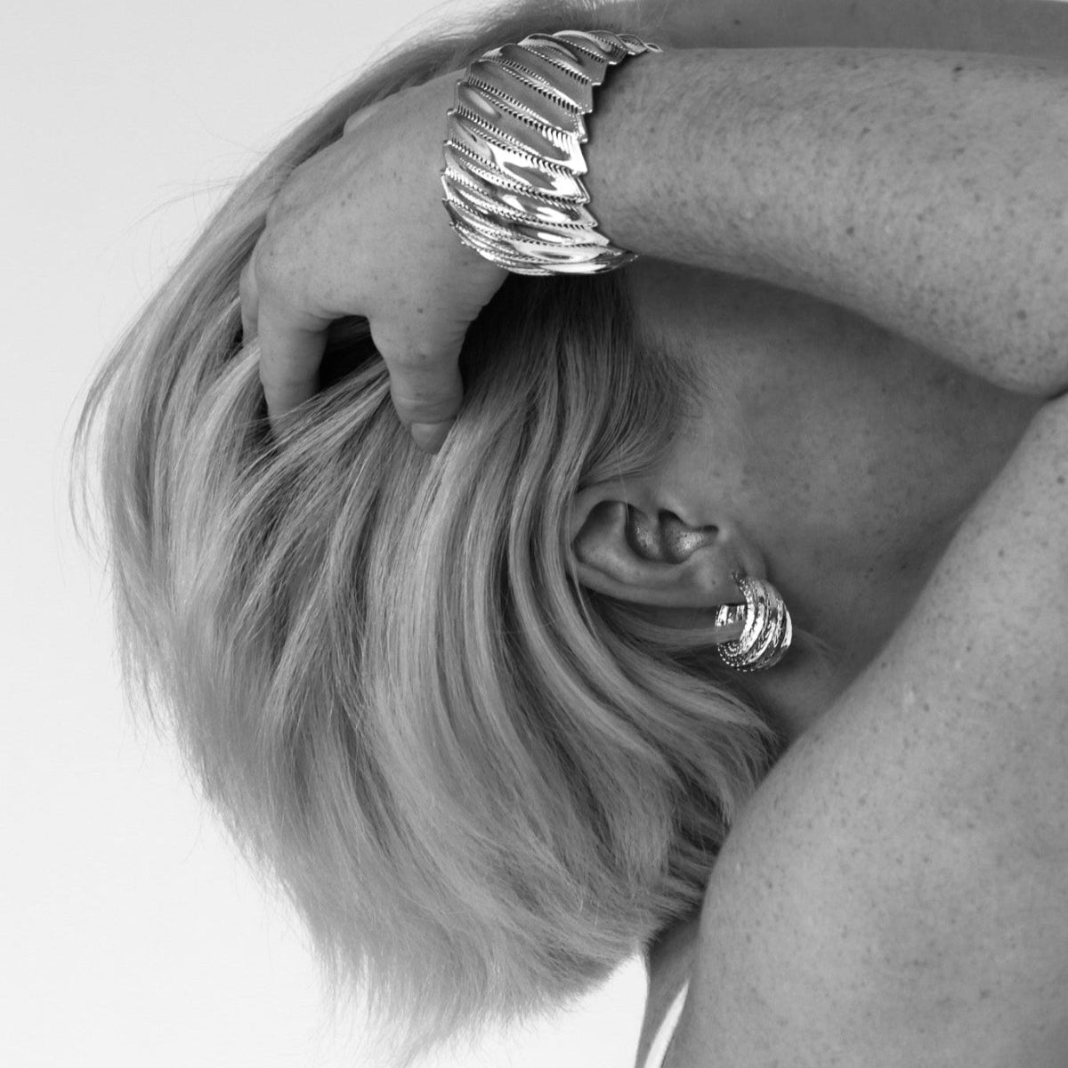 model wearing sculptural gold-tone hoop earrings with flowing ridges.